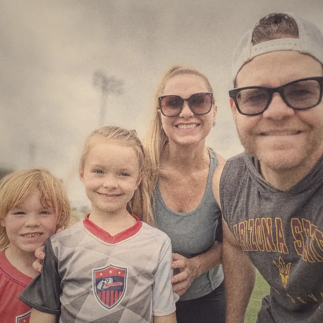 TJ, his wife and their two kids smiling at a soccer field, his daughter in her team jersey